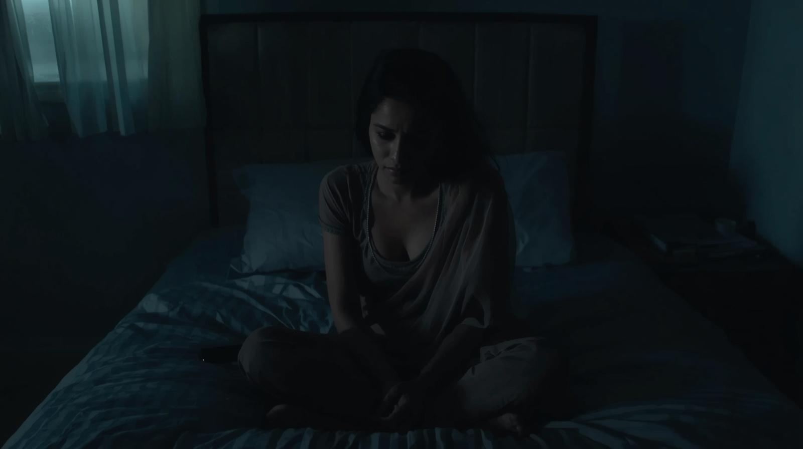 woman sitting on bed at night with phone beside her, room softly lit, emotional but restrained
