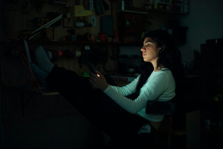 Woman sitting alone at night looking at her phone while deciding whether to call her ex after a breakup