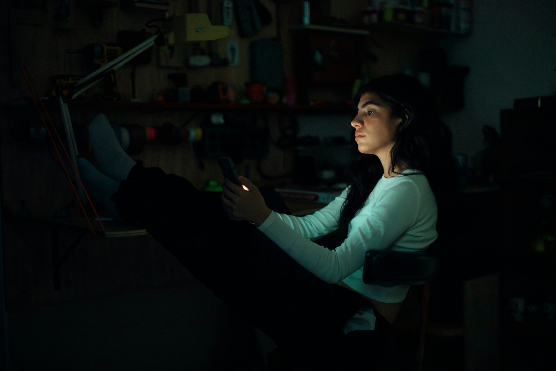 Woman sitting alone at night looking at her phone while deciding whether to call her ex after a breakup