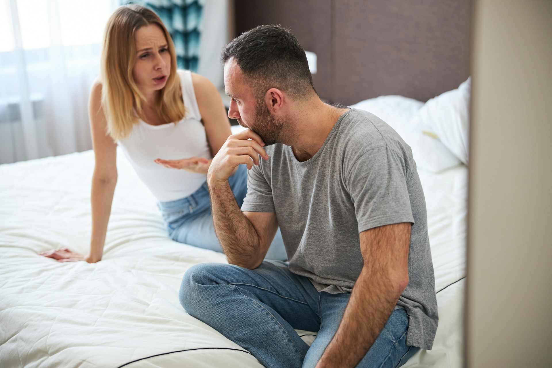 Man sitting apart and looking conflicted while his partner speaks to him, representing fear of commitment, relationship tension and emotional withdrawal as the relationship becomes more serious.