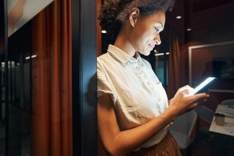 Woman checking her phone while sitting at a café table, representing dating, texting, first dates and early relationship interest.